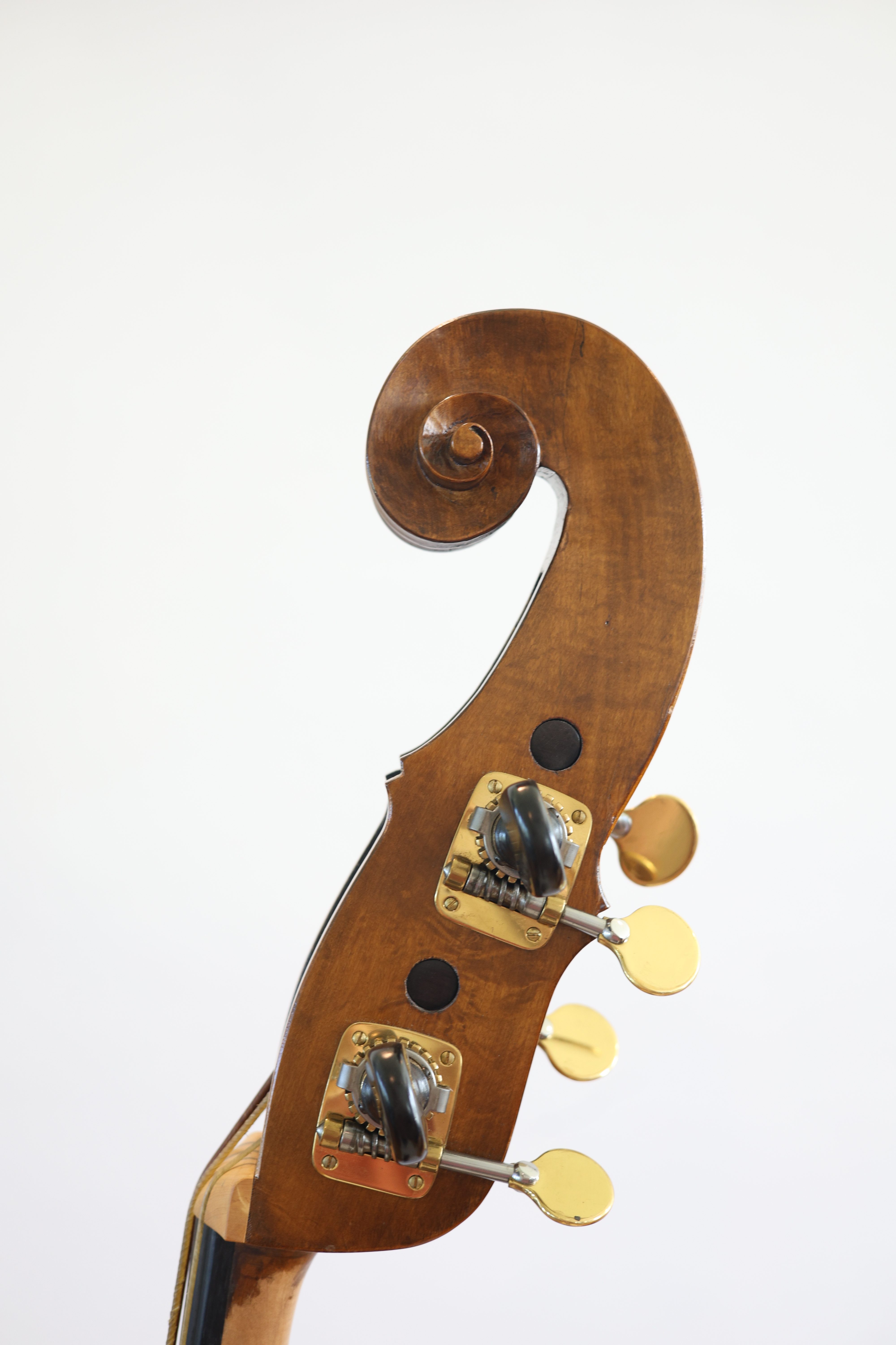 Close-up of the scroll and tuning pegs of a wooden double bass against a white background.